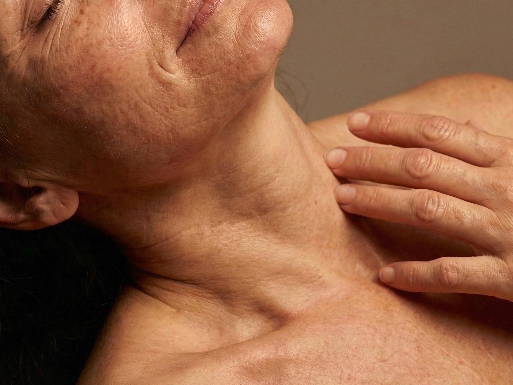 Close-up of a person's neck and shoulder with a hand gently touching the skin.